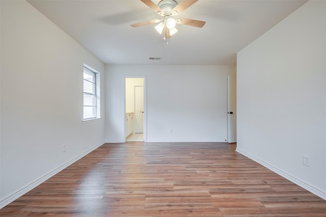 empty room featuring ceiling fan, light wood finished floors, visible vents, and baseboards