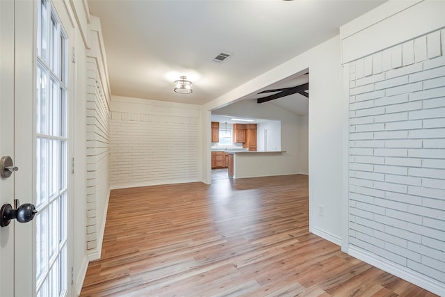 unfurnished living room with light wood-style floors, visible vents, lofted ceiling with beams, and brick wall