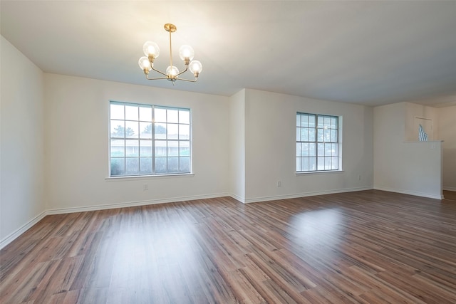 spare room featuring a chandelier, dark wood-style flooring, and baseboards