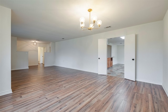 unfurnished room featuring a chandelier, visible vents, baseboards, and wood finished floors