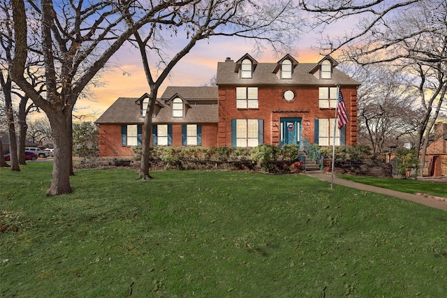 view of front of home with brick siding, a chimney, a front yard, and roof with shingles