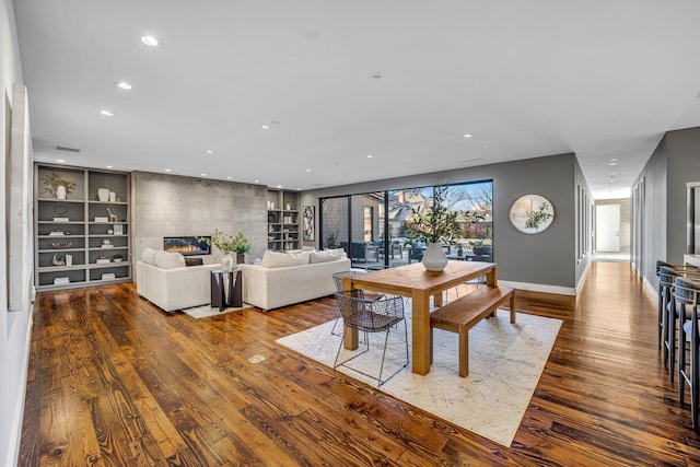 dining room featuring baseboards, wood finished floors, built in shelves, a fireplace, and recessed lighting