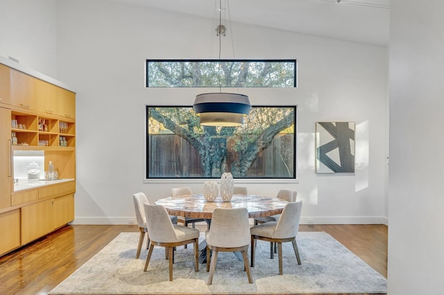 dining area featuring light wood-style floors, high vaulted ceiling, and baseboards