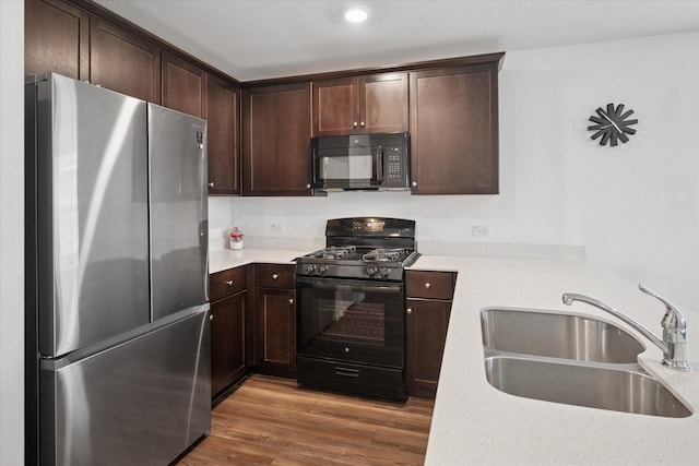 kitchen featuring a sink, black appliances, wood finished floors, and light countertops