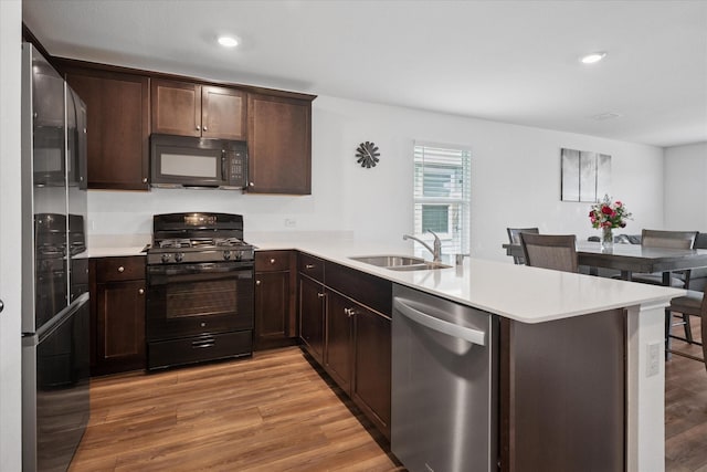 kitchen featuring black appliances, a peninsula, a sink, and light countertops