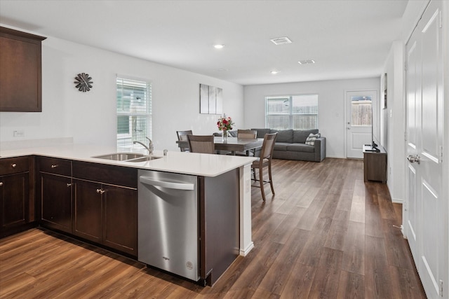 kitchen with light countertops, stainless steel dishwasher, dark wood-type flooring, a sink, and a peninsula