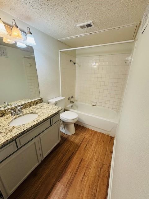 bathroom with shower / bathtub combination, toilet, a textured ceiling, vanity, and wood finished floors