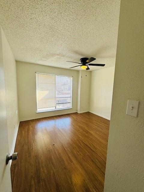 unfurnished room featuring ceiling fan, a textured ceiling, baseboards, and dark wood-type flooring