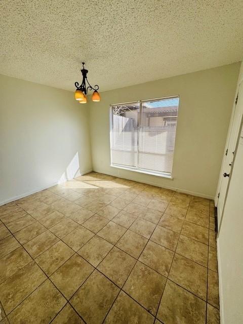 spare room with a chandelier, a textured ceiling, and tile patterned floors