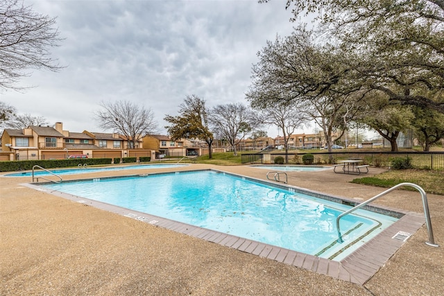 community pool with a residential view, a patio area, and fence