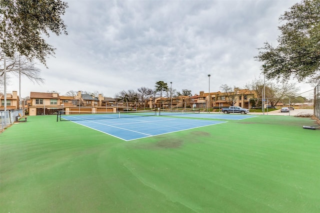 view of tennis court featuring a residential view and fence