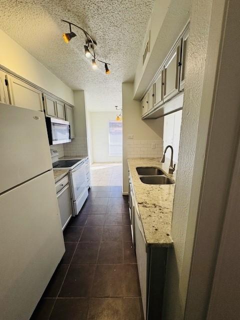 kitchen with a textured ceiling, white appliances, a sink, and decorative backsplash