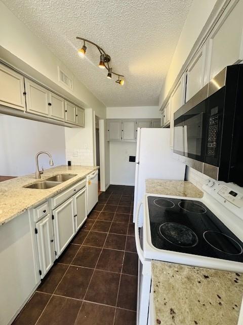 kitchen with white appliances, visible vents, a textured ceiling, dark tile patterned floors, and a sink