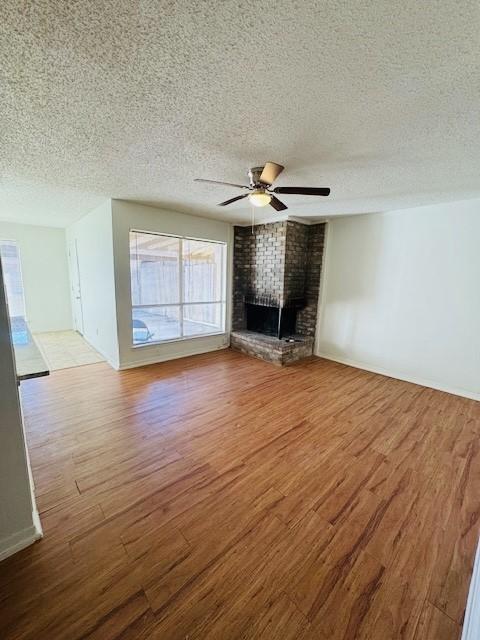 unfurnished living room with ceiling fan, a textured ceiling, a brick fireplace, and wood finished floors