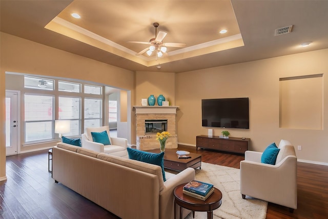 living room featuring a tray ceiling, visible vents, dark wood finished floors, and a fireplace