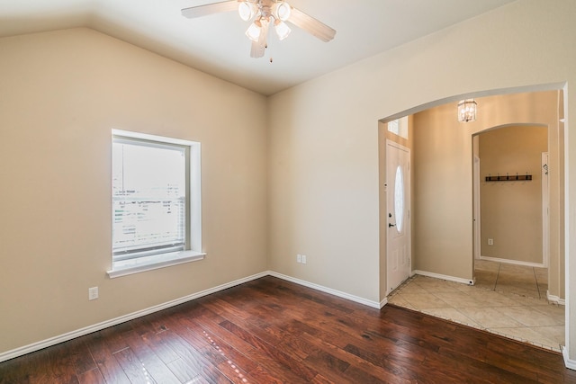 spare room with baseboards, lofted ceiling, hardwood / wood-style flooring, arched walkways, and a ceiling fan