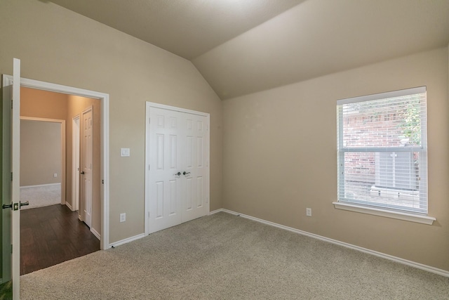 unfurnished bedroom featuring baseboards, lofted ceiling, and dark colored carpet