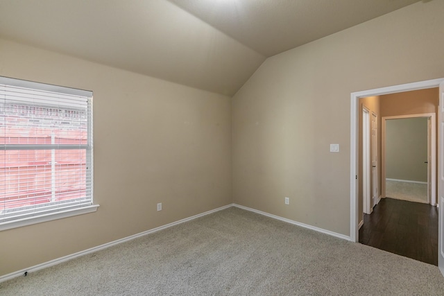 interior space featuring baseboards, dark carpet, and vaulted ceiling