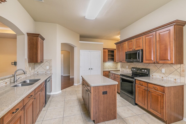 kitchen with light tile patterned floors, light stone countertops, a kitchen island, a sink, and stainless steel appliances