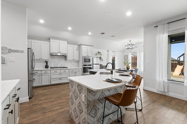 kitchen with a breakfast bar area, a kitchen island with sink, stainless steel appliances, a sink, and backsplash