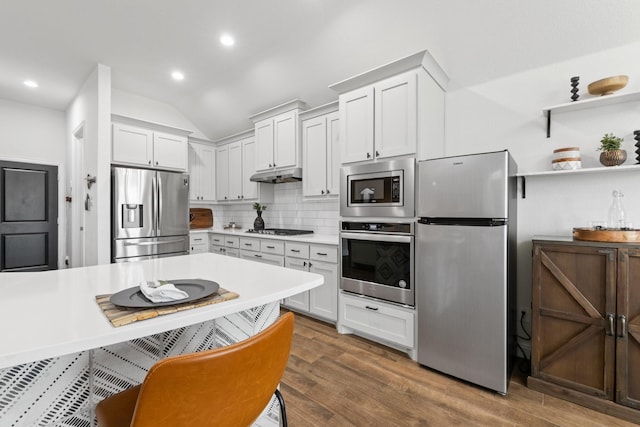 kitchen featuring stainless steel appliances, light countertops, decorative backsplash, wood finished floors, and under cabinet range hood