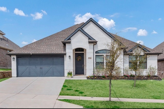 french country home with a garage, a front yard, driveway, and brick siding