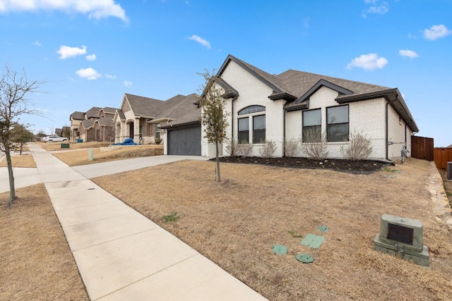 french provincial home featuring an attached garage, brick siding, a shingled roof, fence, and concrete driveway