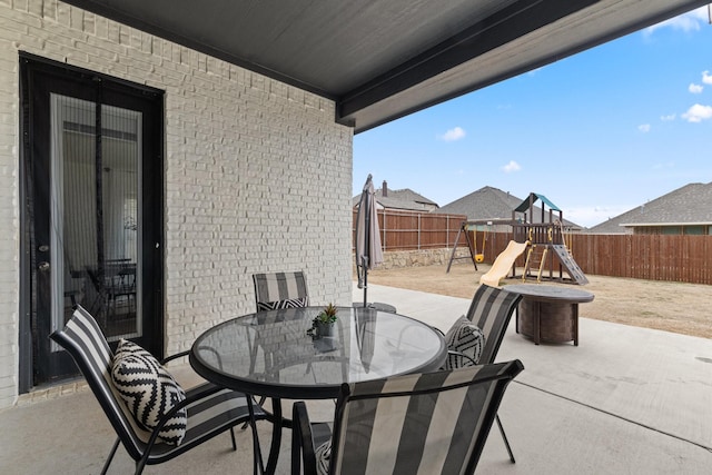 view of patio / terrace featuring outdoor dining space, a playground, and a fenced backyard