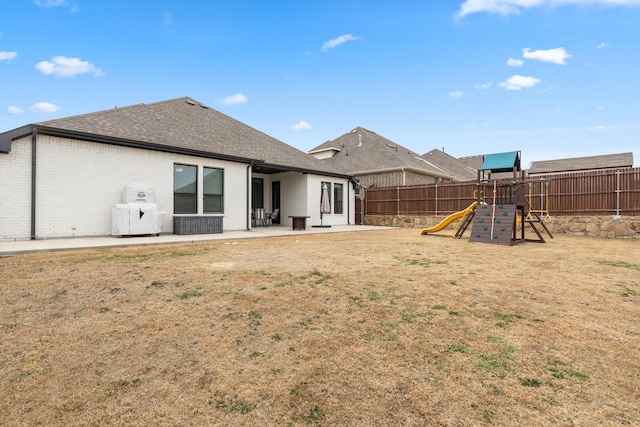 back of property with a patio, a playground, brick siding, fence, and roof with shingles