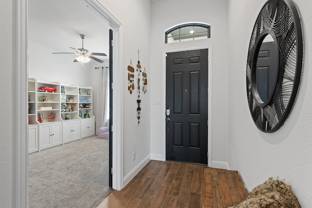 entrance foyer featuring dark wood-type flooring, dark carpet, a ceiling fan, and baseboards