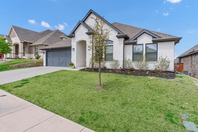 french country style house with driveway, roof with shingles, brick siding, a front lawn, and an attached garage