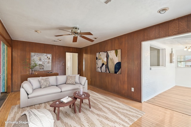 living room with light wood-type flooring, wood walls, and ceiling fan