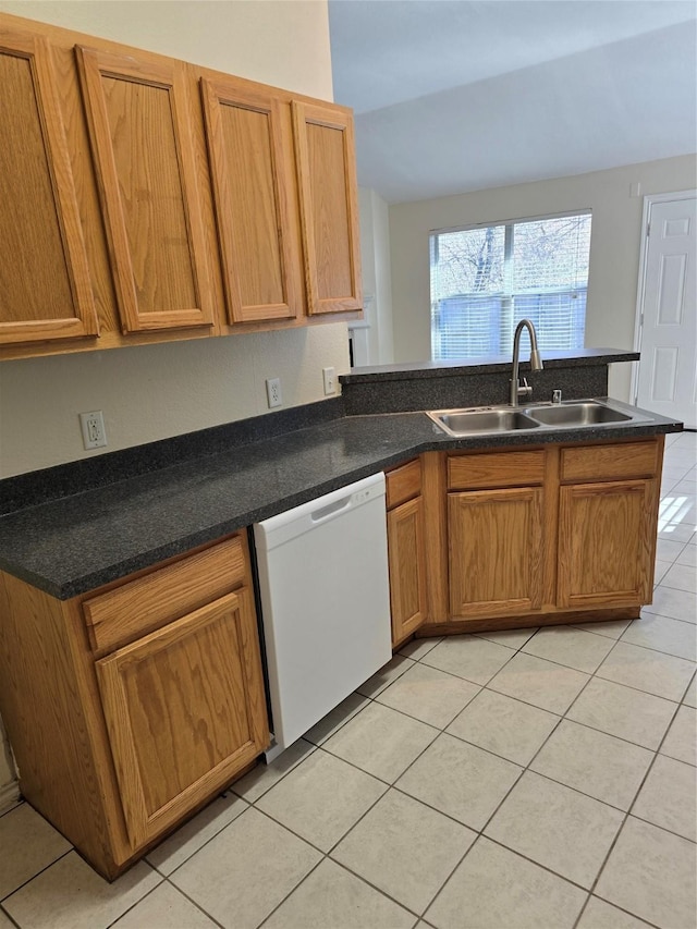 kitchen featuring brown cabinets, light tile patterned floors, dark countertops, white dishwasher, and a sink