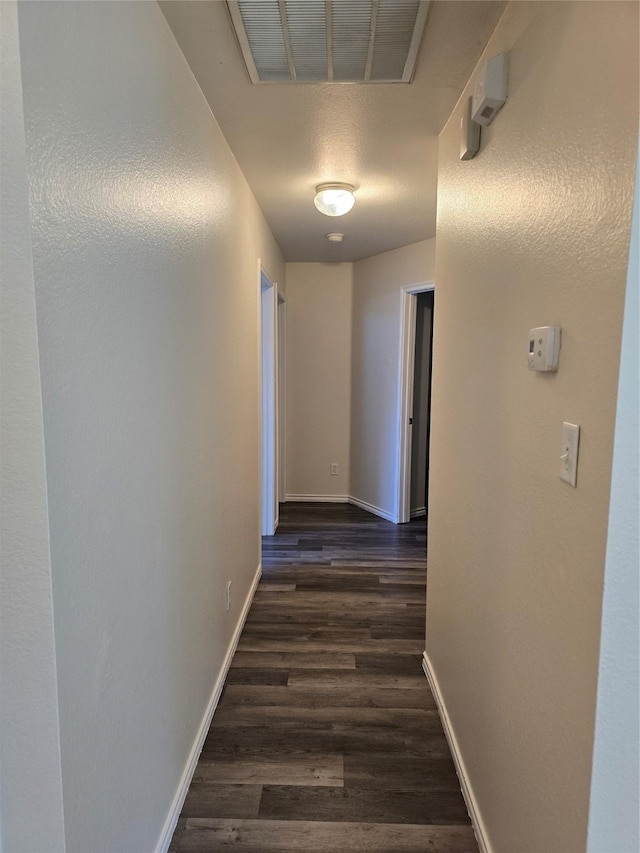 corridor with dark wood-type flooring, visible vents, and baseboards