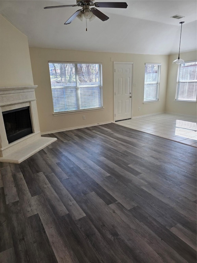 unfurnished living room with visible vents, vaulted ceiling, dark wood finished floors, and a high end fireplace