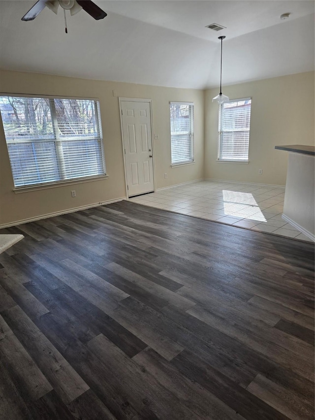 unfurnished living room featuring baseboards, visible vents, a ceiling fan, dark wood-style floors, and vaulted ceiling