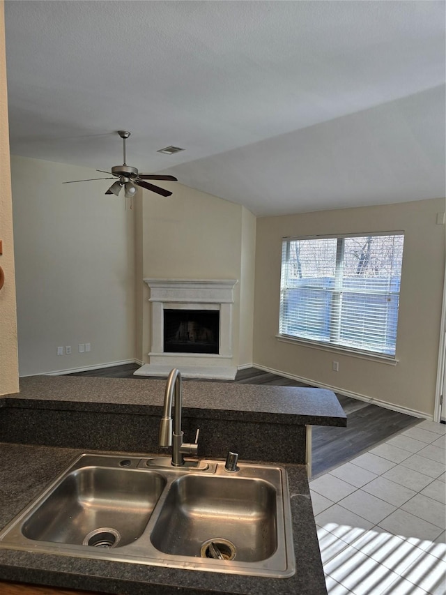 kitchen featuring visible vents, a fireplace with raised hearth, dark countertops, lofted ceiling, and a sink