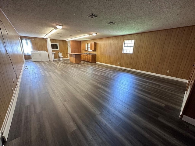 unfurnished living room with a healthy amount of sunlight, visible vents, dark wood finished floors, and washer and clothes dryer