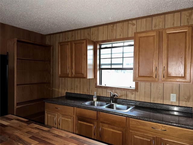 kitchen featuring brown cabinets, a sink, wooden walls, and a textured ceiling