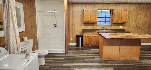 interior space with toilet, washer / clothes dryer, wood finished floors, a shower stall, and a sink