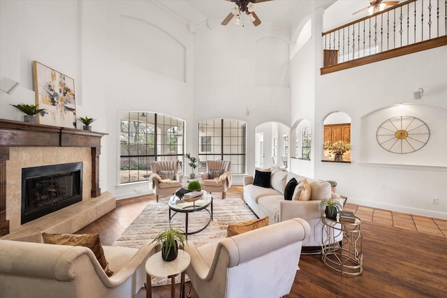 living area featuring a ceiling fan, a tile fireplace, baseboards, and wood finished floors