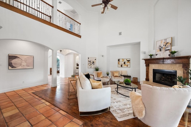 living room with arched walkways, a tile fireplace, a ceiling fan, and baseboards