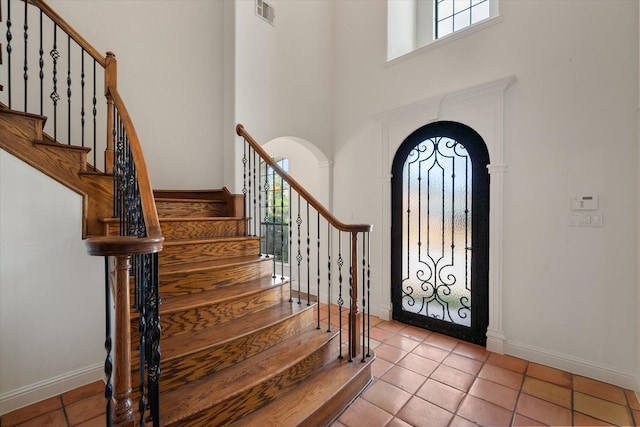 tiled foyer entrance with arched walkways, a high ceiling, visible vents, and baseboards