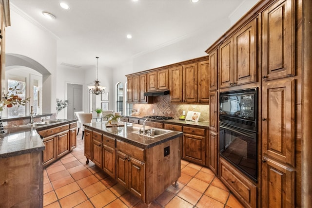 kitchen featuring a kitchen island with sink, a sink, brown cabinets, black appliances, and tasteful backsplash