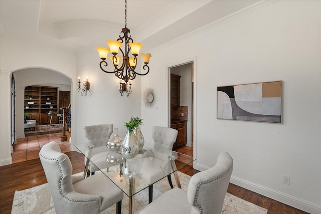 dining space with baseboards, arched walkways, wood finished floors, a tray ceiling, and a chandelier