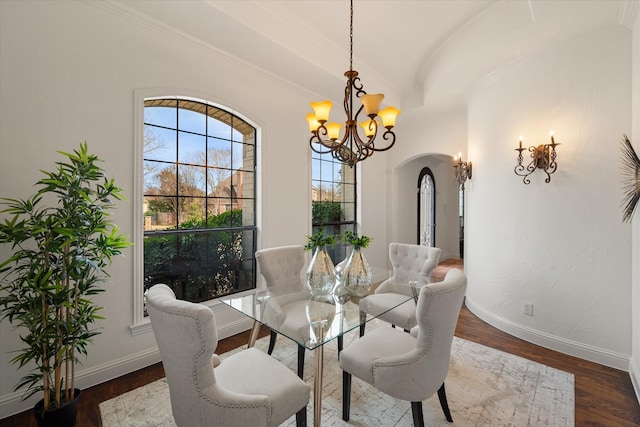 dining area with baseboards, arched walkways, wood finished floors, vaulted ceiling, and a chandelier