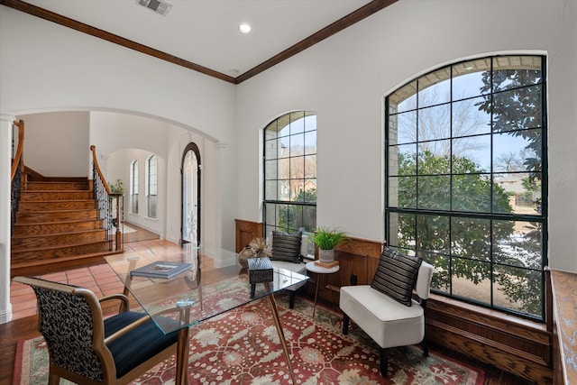 living area with arched walkways, visible vents, ornamental molding, wood finished floors, and stairs