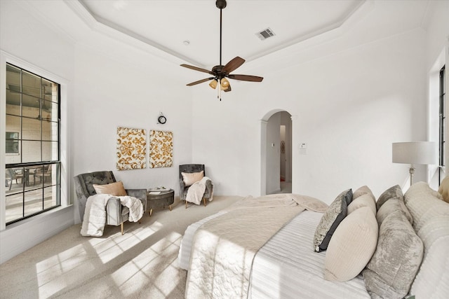 carpeted bedroom featuring arched walkways, a raised ceiling, visible vents, and a ceiling fan