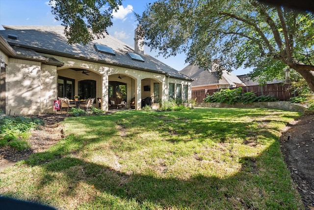 rear view of house with fence, a ceiling fan, a yard, a chimney, and a patio area