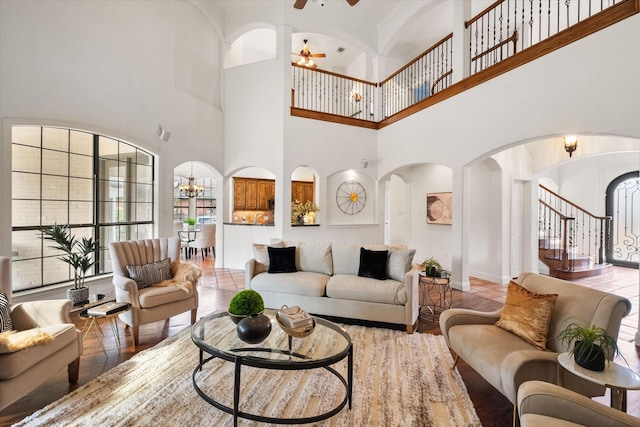 living area featuring ceiling fan with notable chandelier, stairway, arched walkways, and baseboards